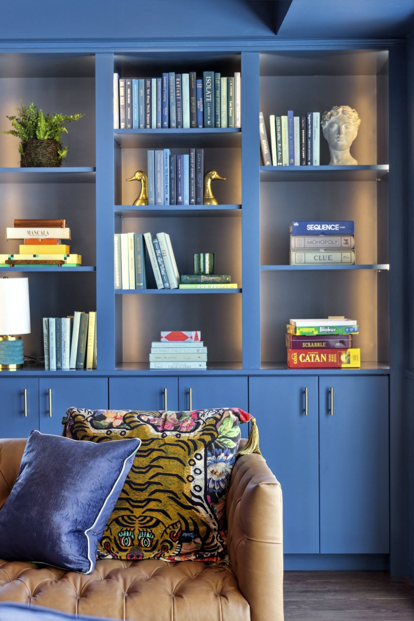 Blue built-in bookcase wall filled with books and decor behind a tufted tan sofa at Esox House in St. Paul, MN.
