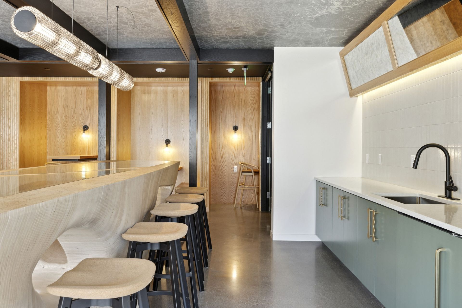 Modern apartment kitchen with a curved wood bar, stools, and pendant lighting at Esox House in St. Paul, MN.