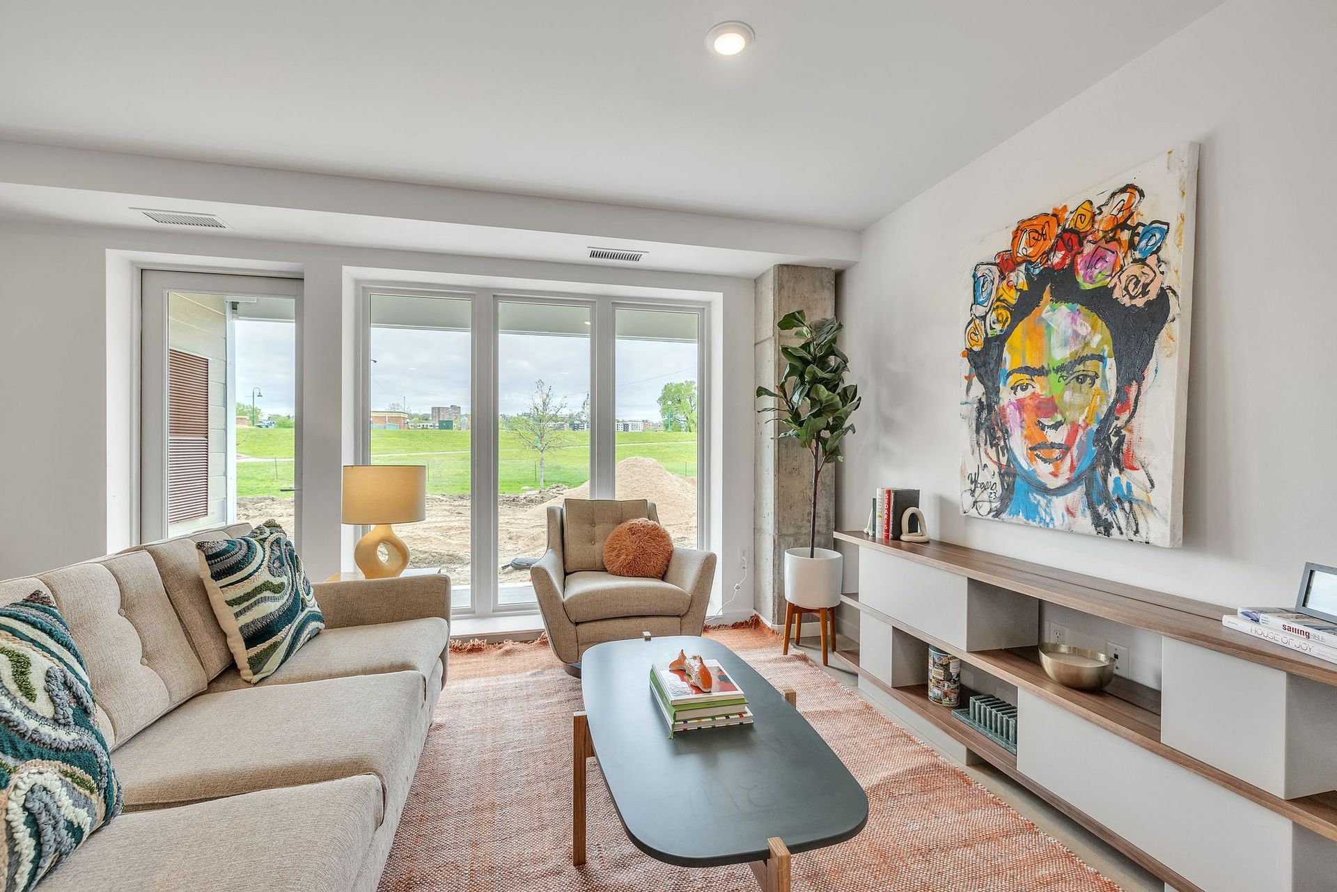 Bright living room with beige sofa, armchair, coffee table, and large windows at Esox House in St. Paul, MN.