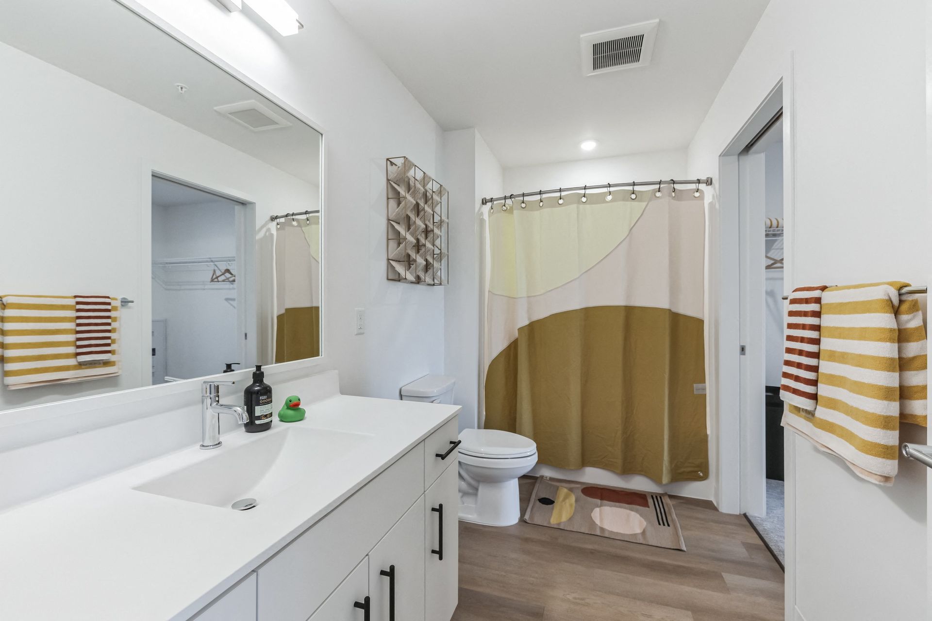 White bathroom with a double-sink vanity, large mirror, toilet, and beige-yellow shower curtain at Esox House in St. Paul, MN.