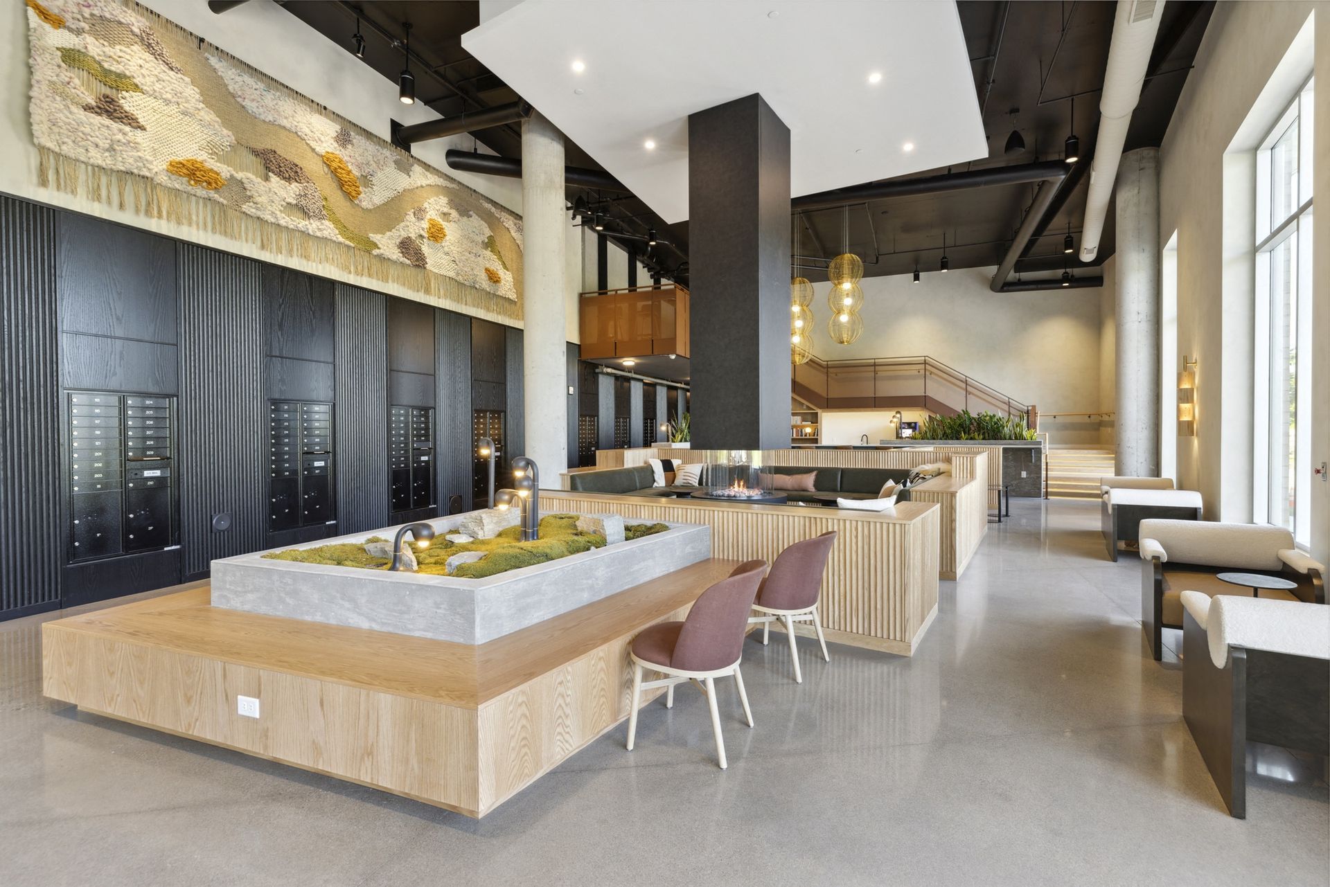 Modern apartment lobby with seating, mailboxes along a dark wall, and a central fireplace at Esox House in St. Paul, MN.
