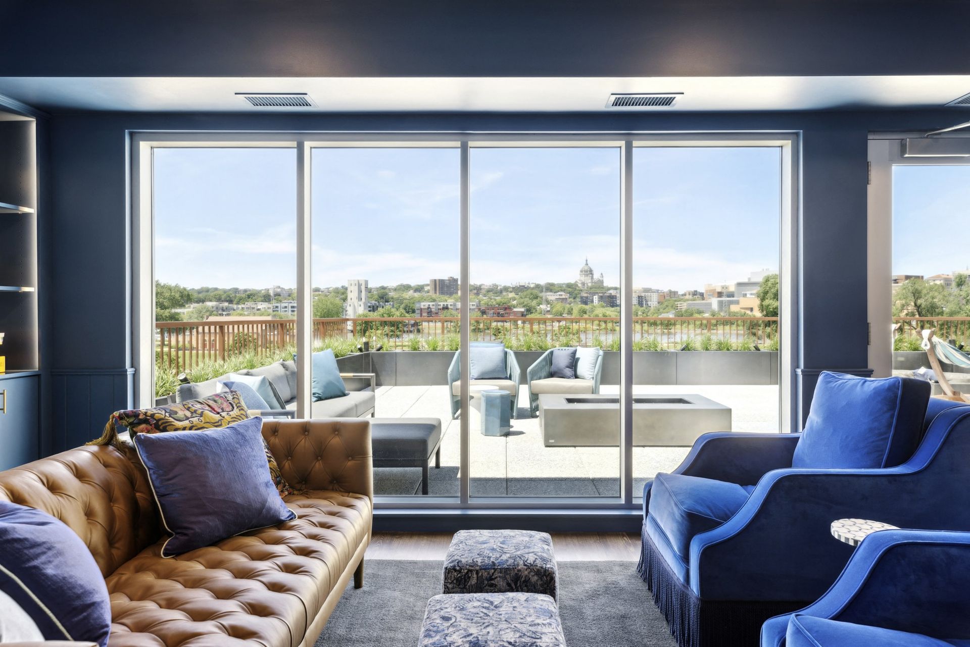 Living room with tan tufted sofa, blue chairs, and a sliding glass door to a balcony at Esox House in St. Paul, MN.