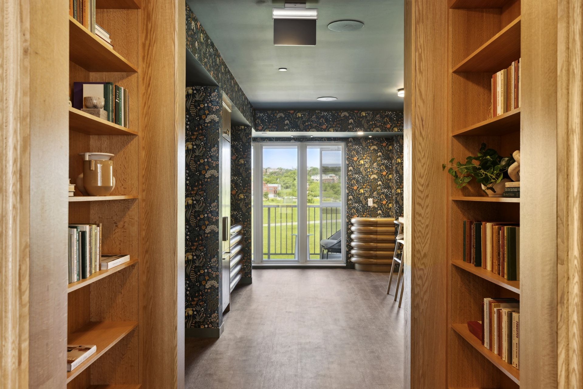 Interior community lounge with floor-to-ceiling bookshelves on both sides and floral wallpaper at Esox House in St. Paul, MN.