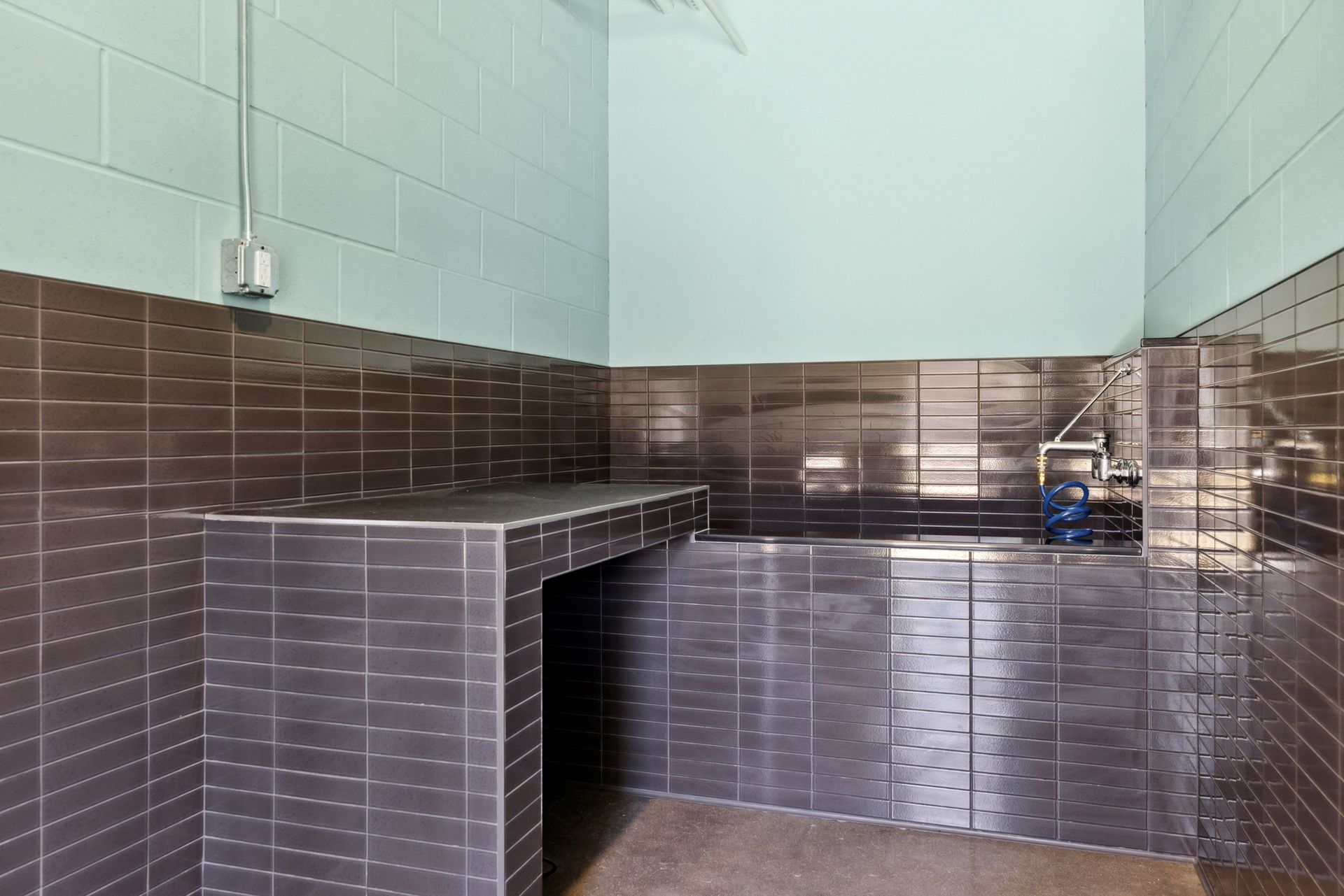Utility area with dark tile walls, a counter, and a blue coiled hose at Esox House in St. Paul, MN.