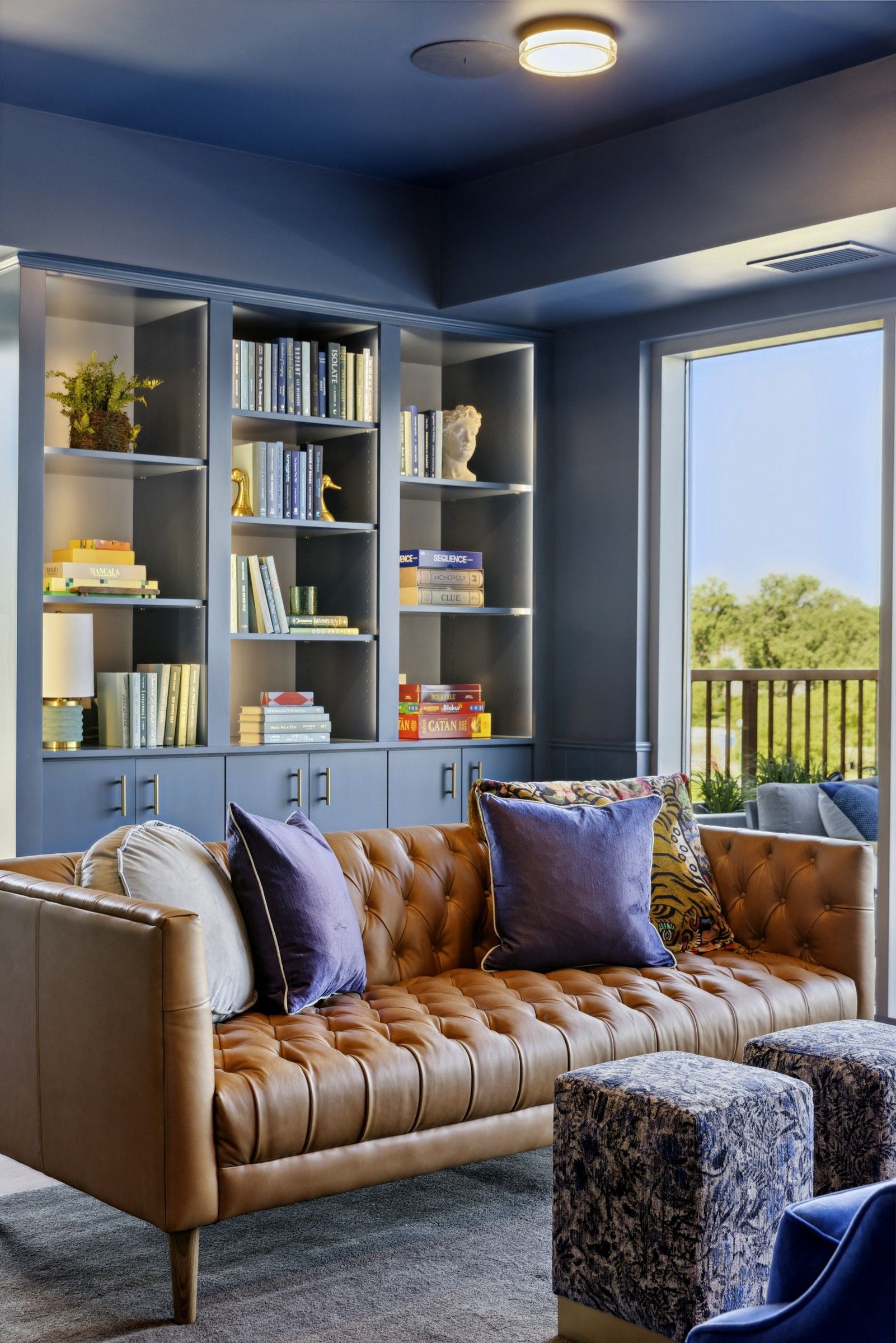 Blue-walled living room with built-in bookshelves, a tan tufted sofa, and a balcony view at Esox House in St. Paul, MN.