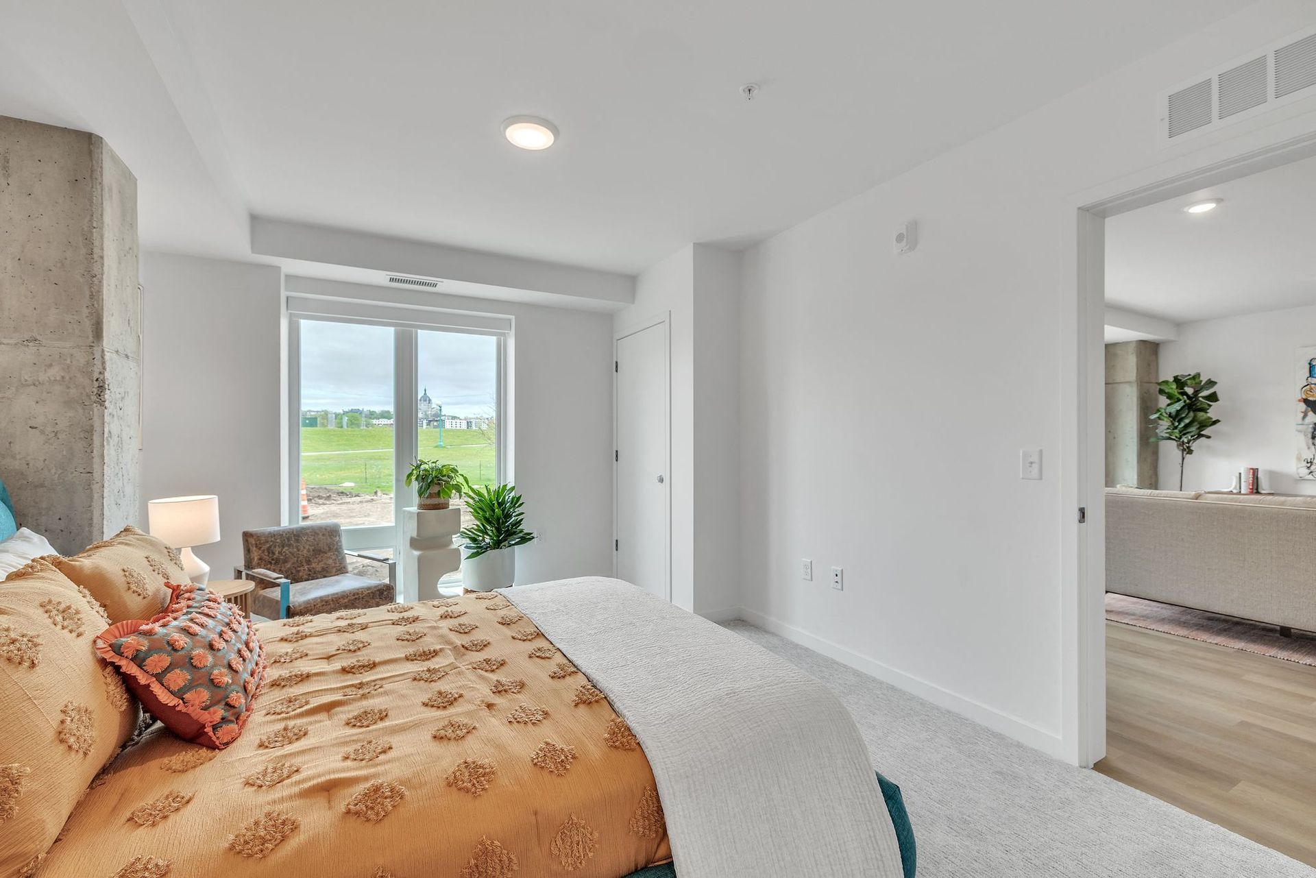 Bedroom in a modern apartment with a bed, two plants, and a large window at Esox House in St. Paul, MN.