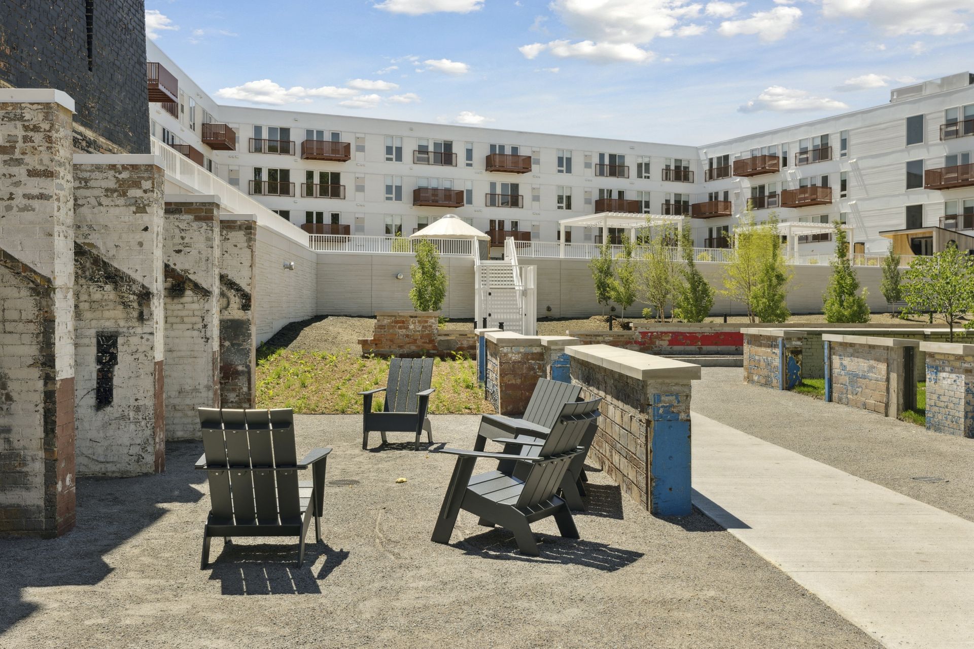 Outdoor communal courtyard with black chairs and brick planters, with a white apartment building in the background at Esox House in St. Paul, MN.