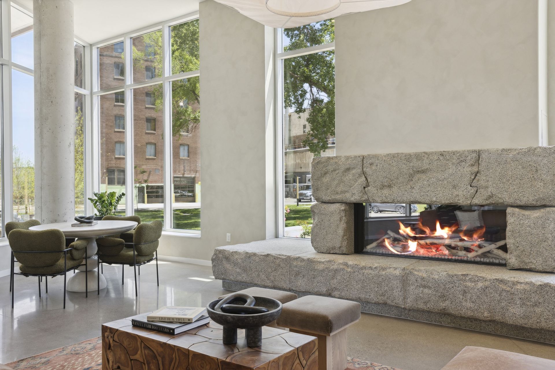 Bright community lounge with floor-to-ceiling windows, a large stone fireplace, and round seating at Esox House in St. Paul, MN.