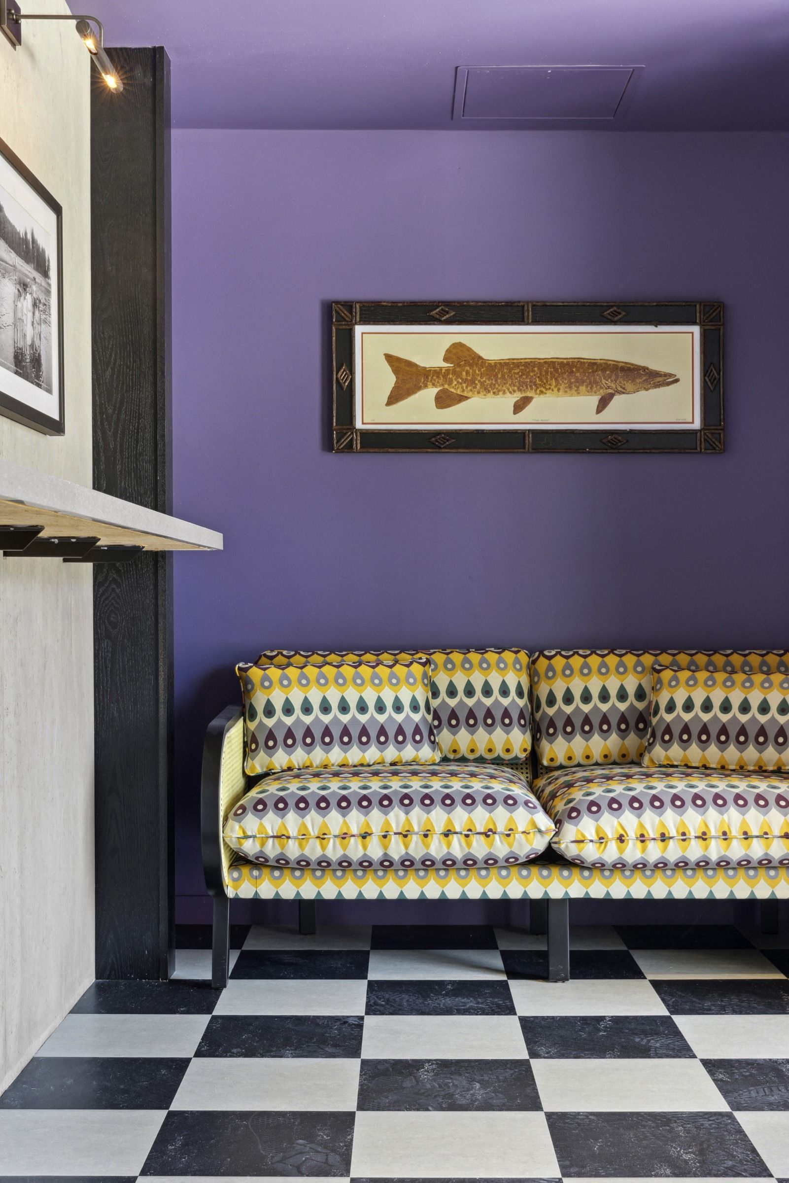Indoor lounge area with purple wall, patterned yellow couch, black-and-white checker floor, framed fish artwork at Esox House in St. Paul, MN.