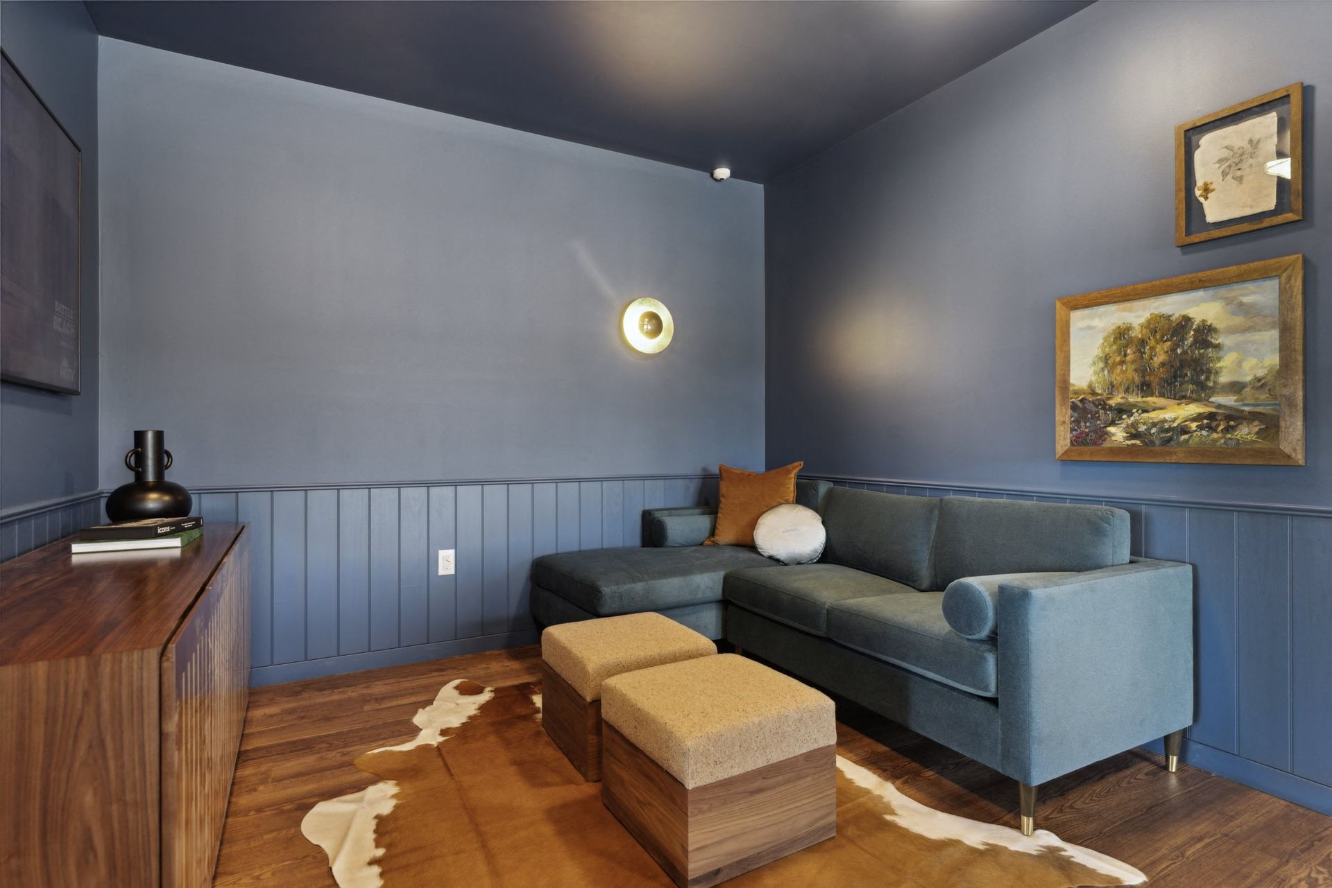 Blue living room in an apartment with a sectional sofa, two ottomans, and framed artwork at Esox House in St. Paul, MN.