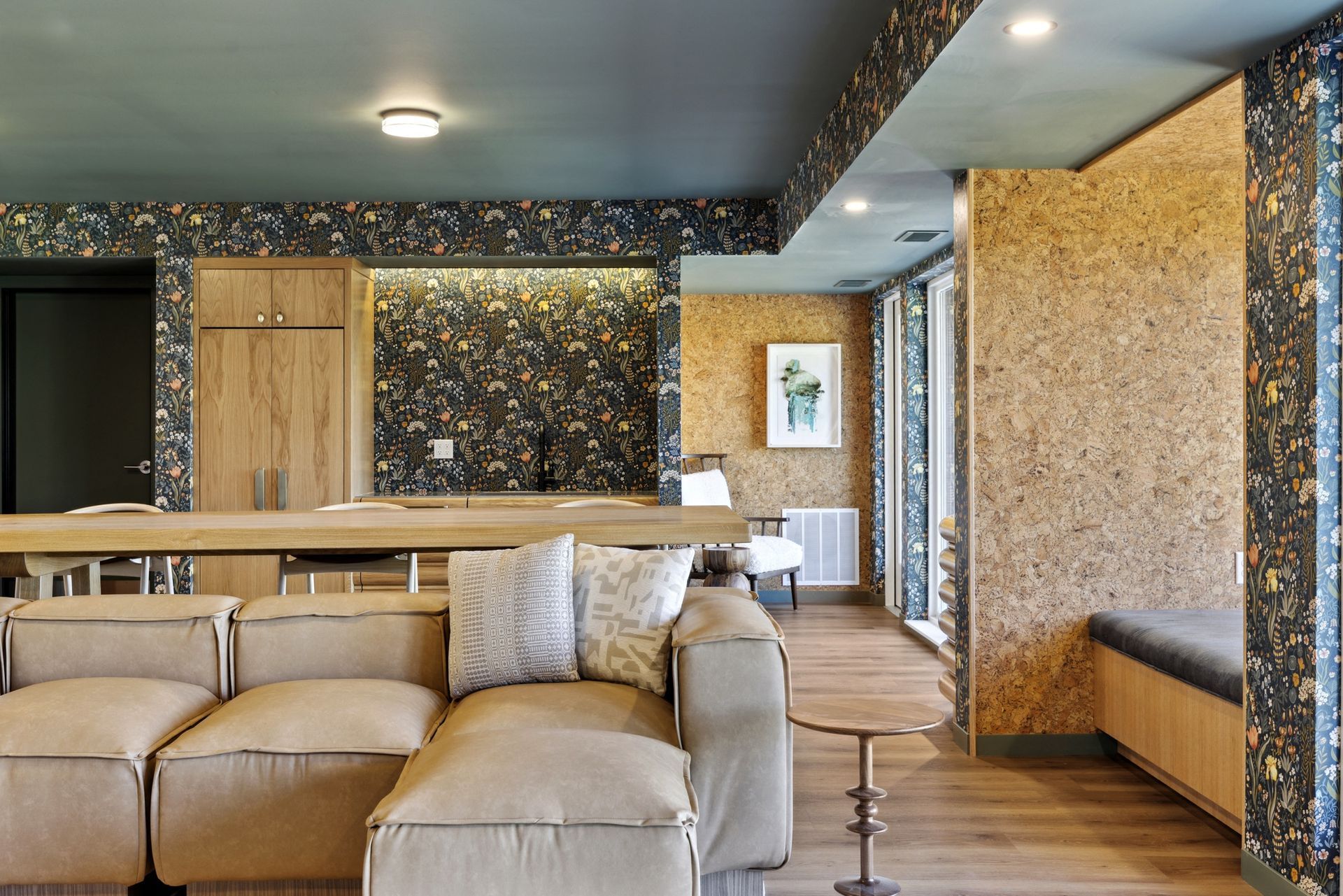 Living room of a modern apartment with a beige leather sofa, wooden tables, and floral wallpaper at Esox House in St. Paul, MN.