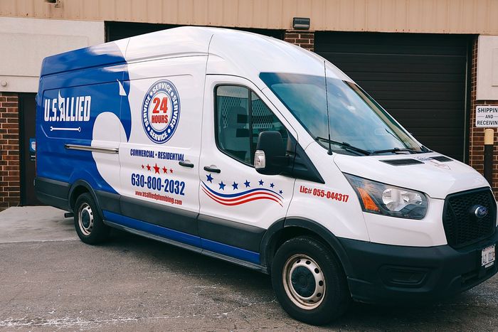 A worker in a lift basket is working on a tall light pole against a blue cloudy sky.