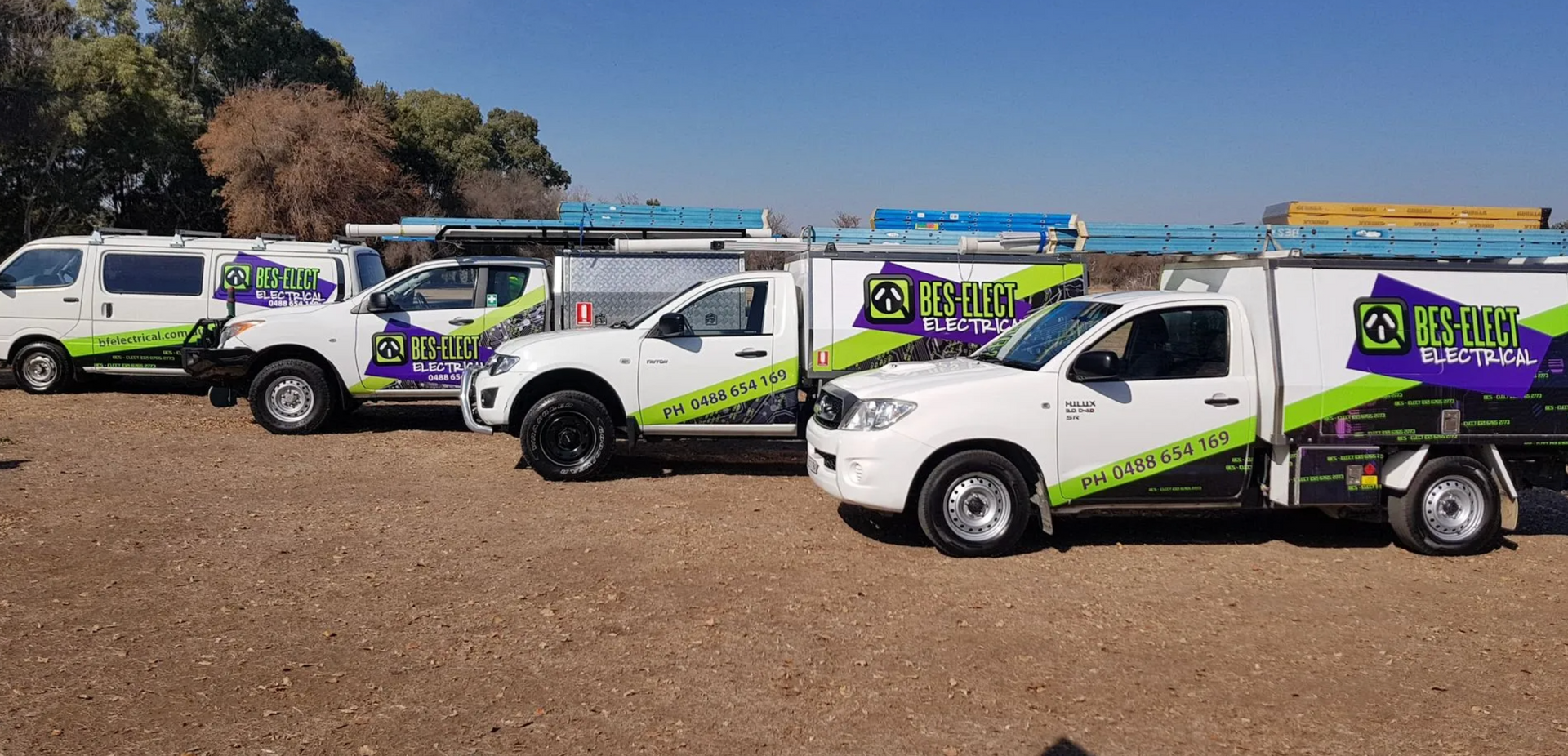Four BF Electrical branded vehicles parked side by side on vacant dirt lot. 