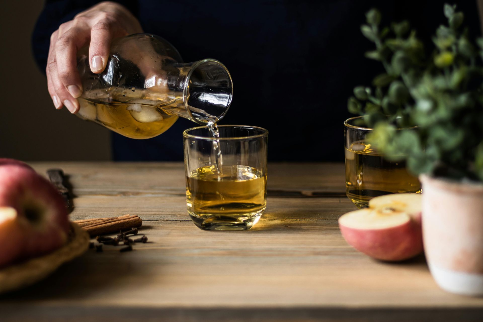 A person is pouring apple cider into a glass on a wooden table.