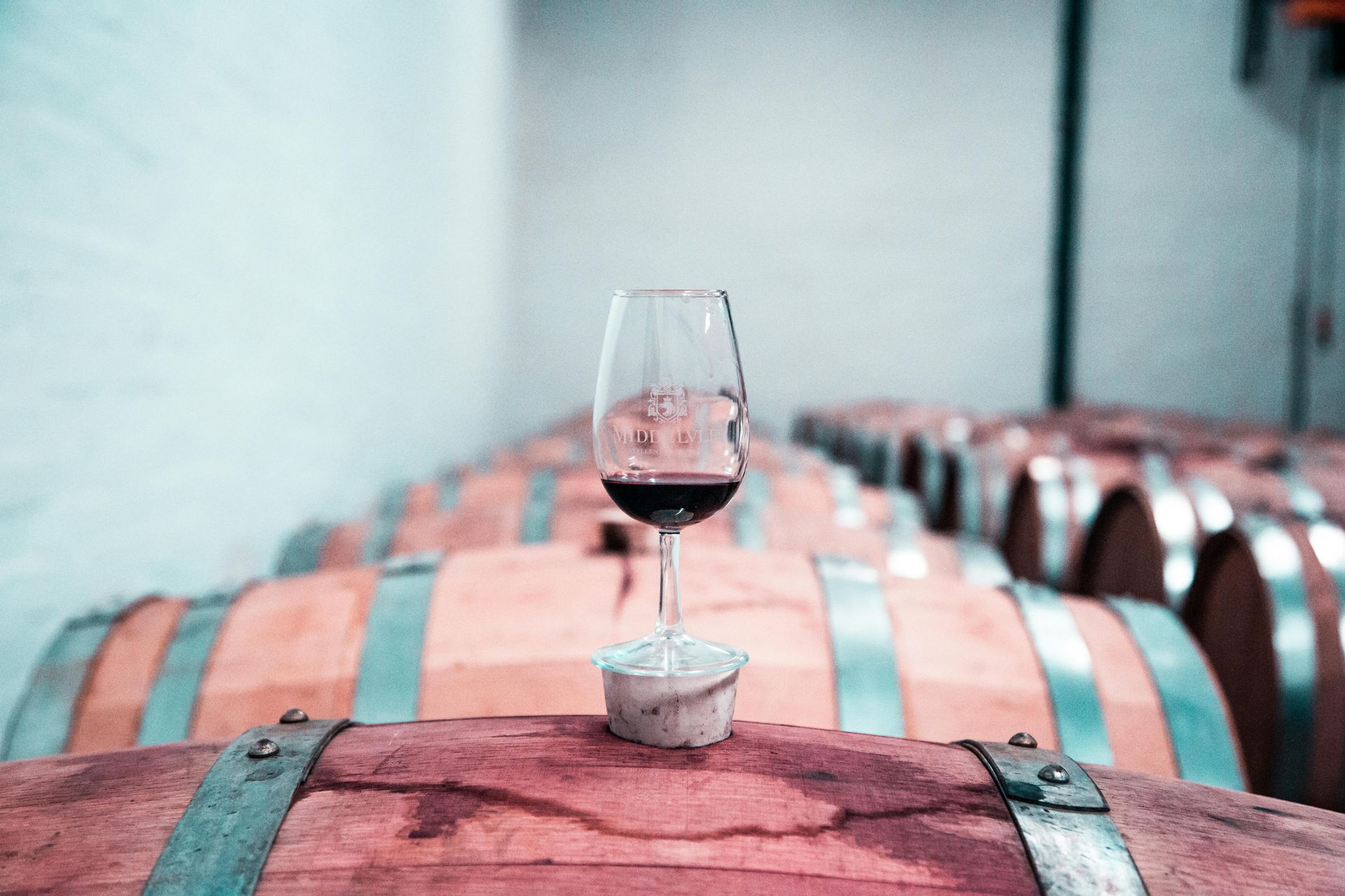 A glass of wine is sitting on top of a wooden barrel in a wine cellar.