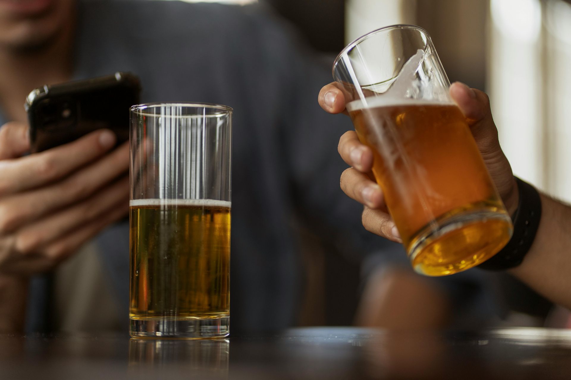 A man is holding a glass of beer while looking at his phone.