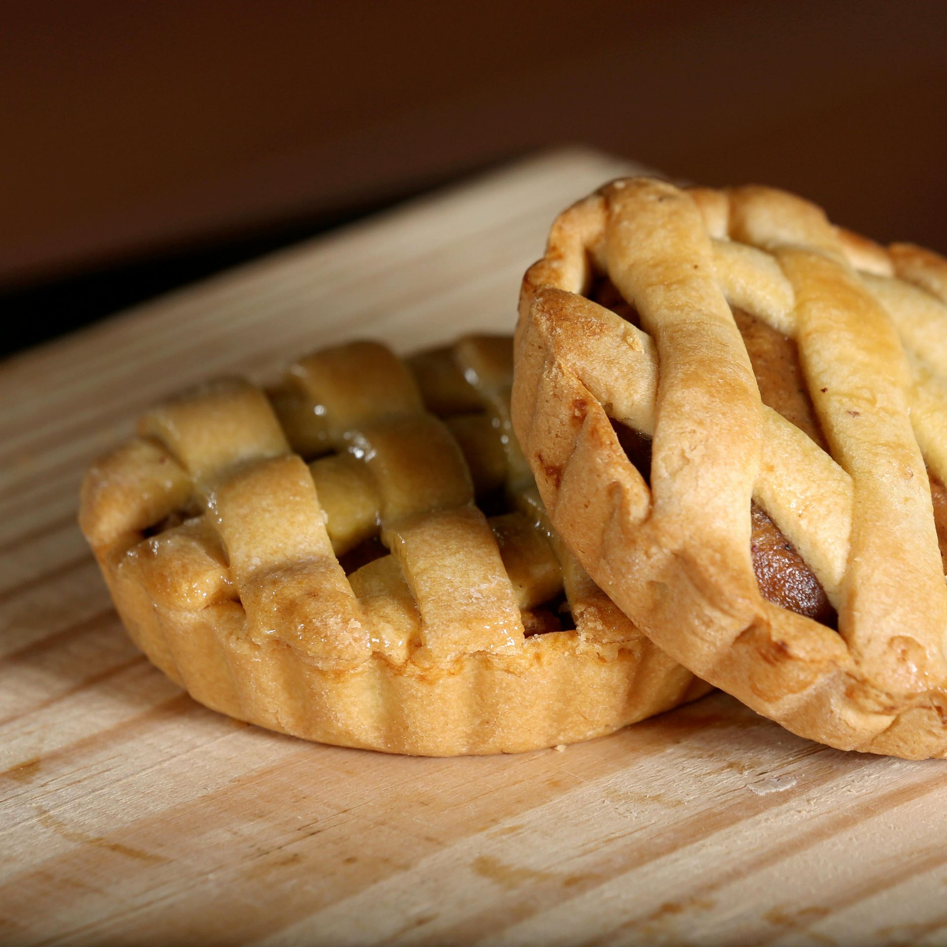 Two small apple pies with lattice crust on a wooden board.