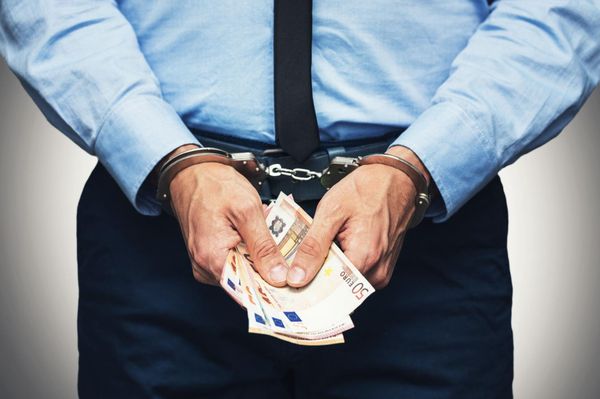 A man in handcuffs is holding a bunch of money in his hands.