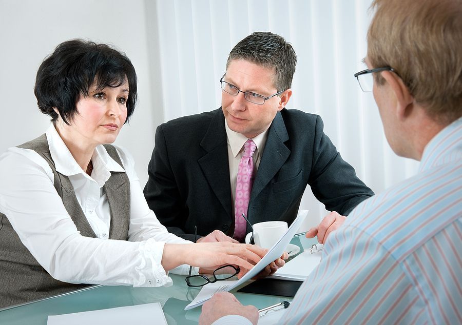 A man and a woman are sitting at a table talking to a man.