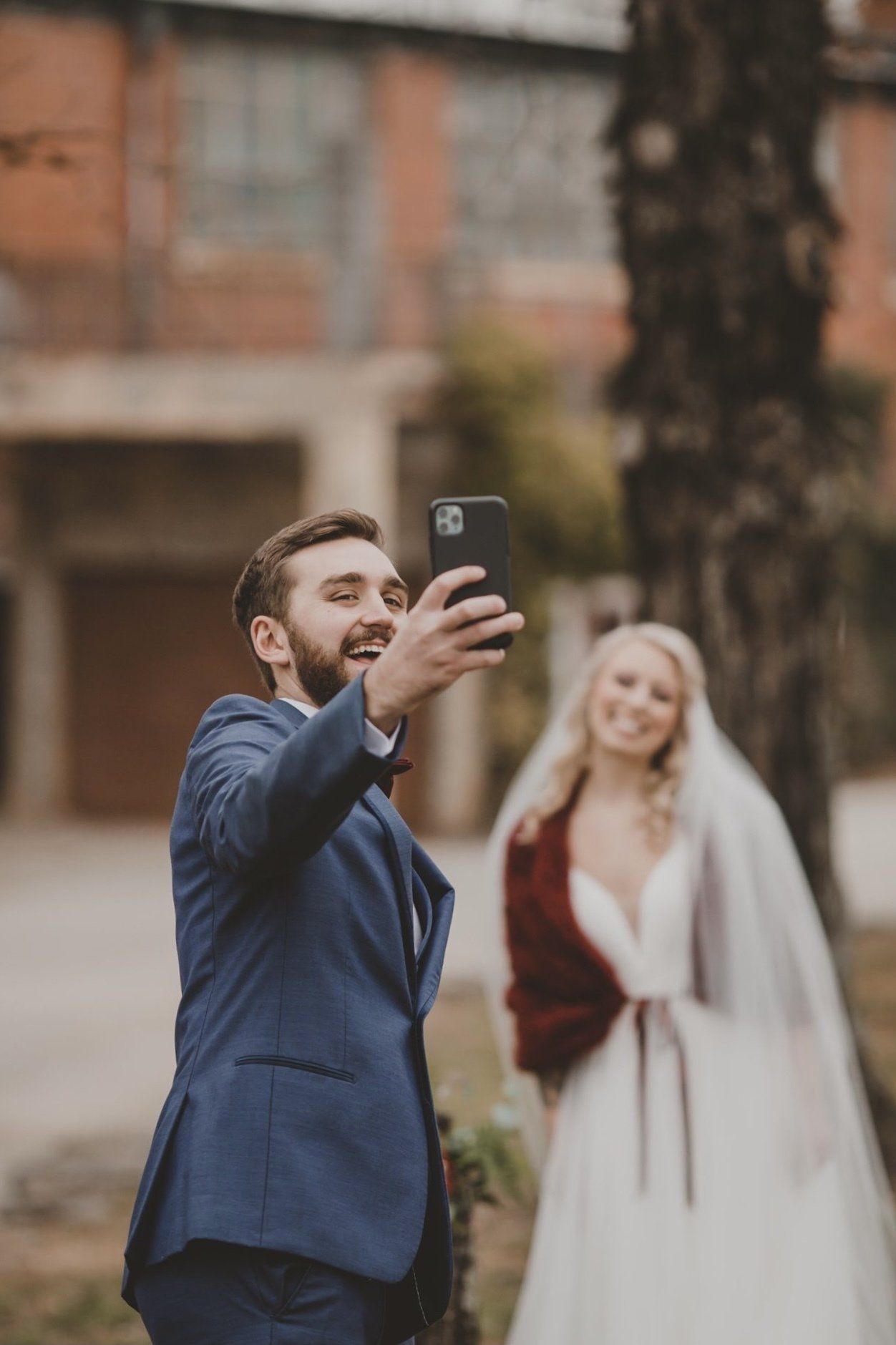 A man in a suit is taking a selfie with a bride in a wedding dress.