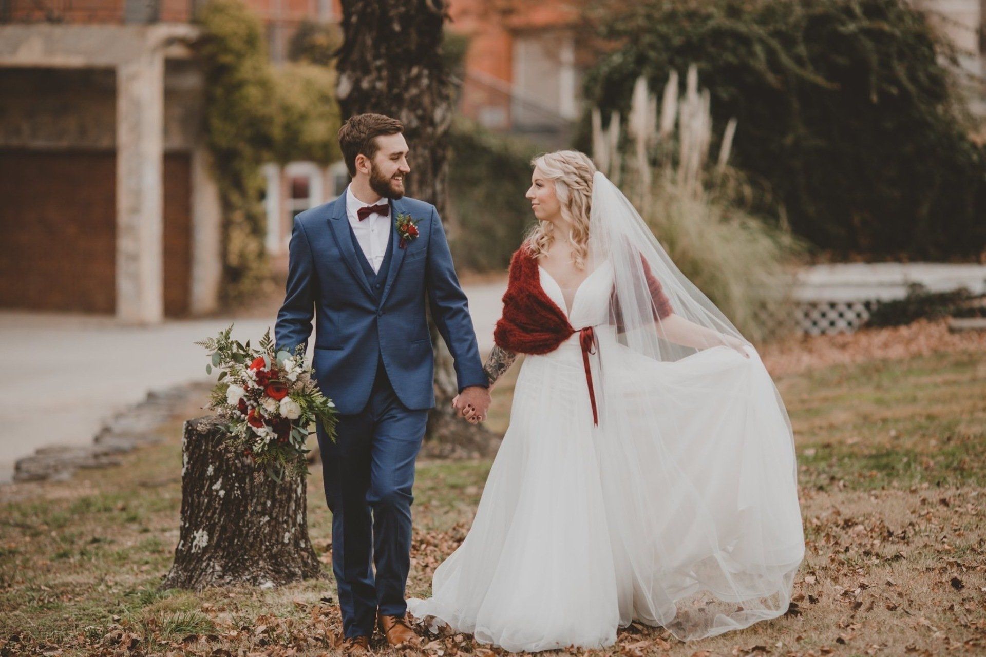 A bride and groom are walking in a field holding hands.