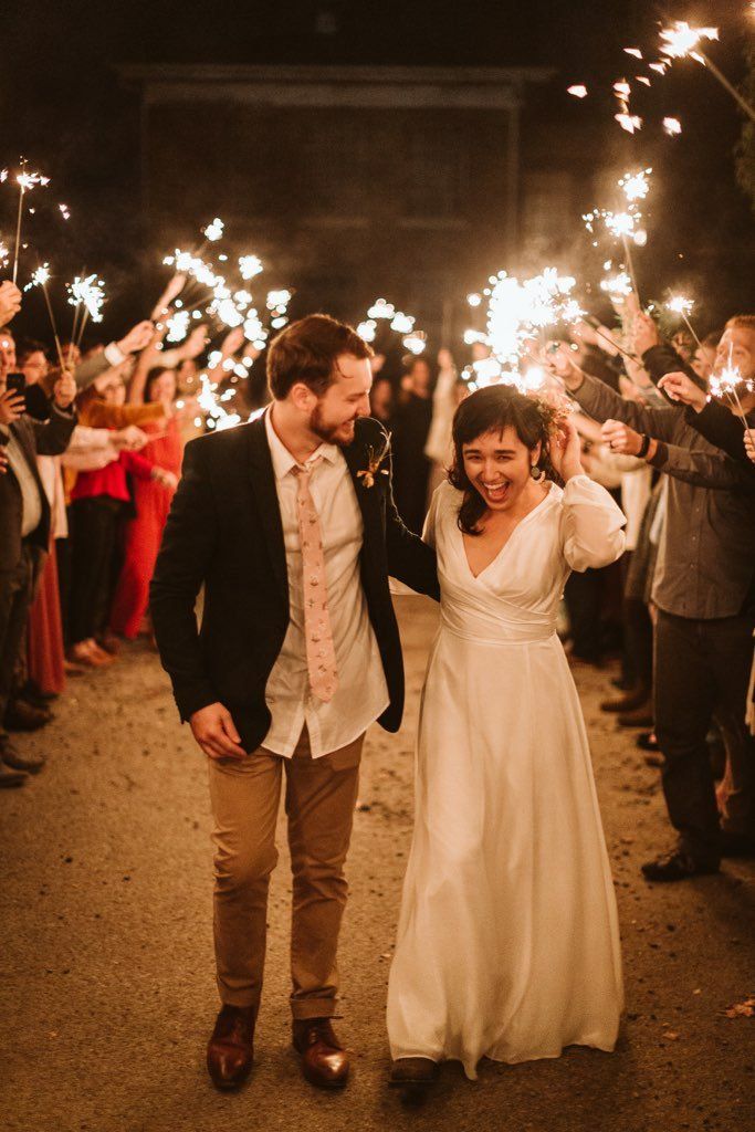 A bride and groom are walking through a tunnel of sparklers.