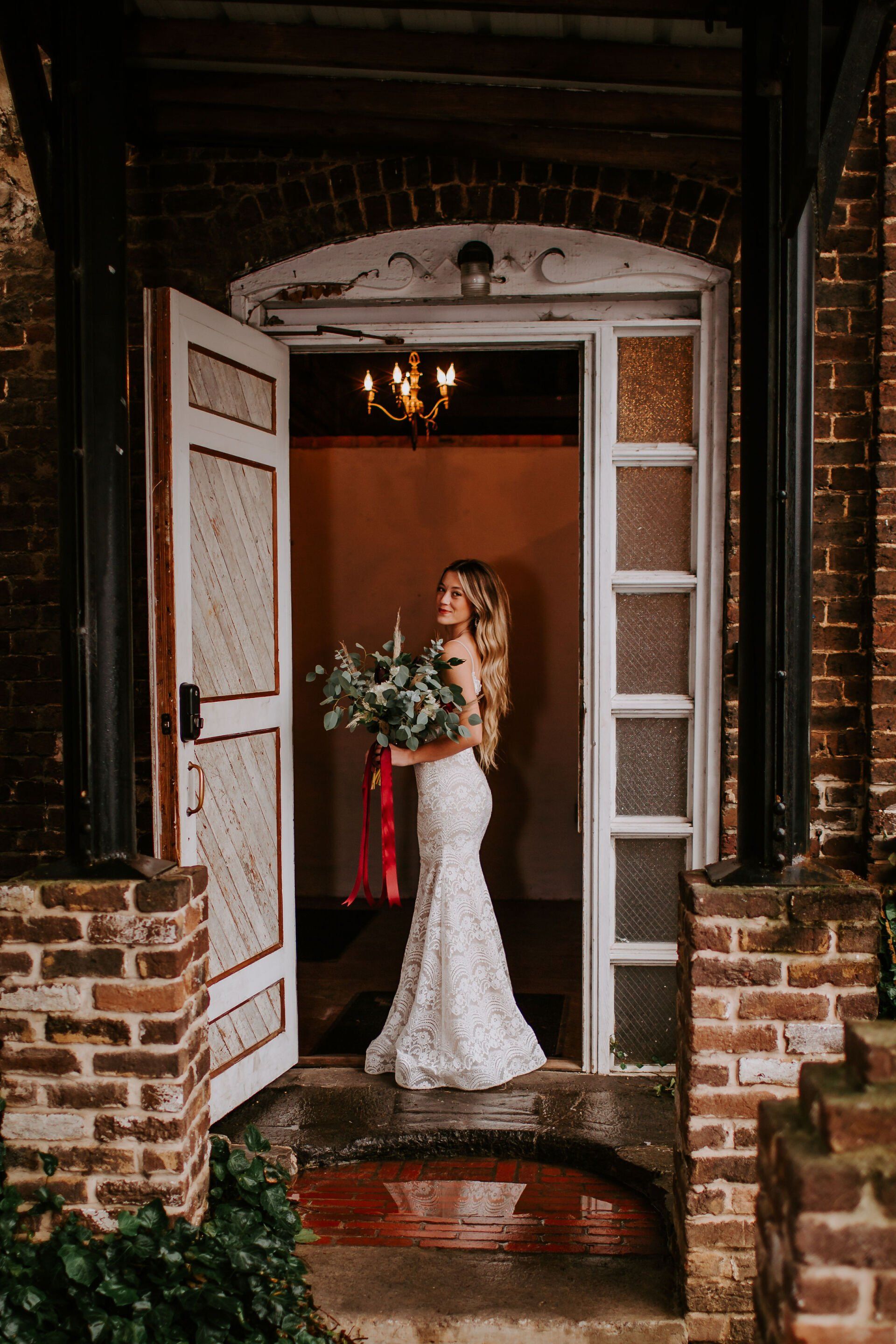 A bride in a wedding dress is standing in a doorway holding a bouquet of flowers.
