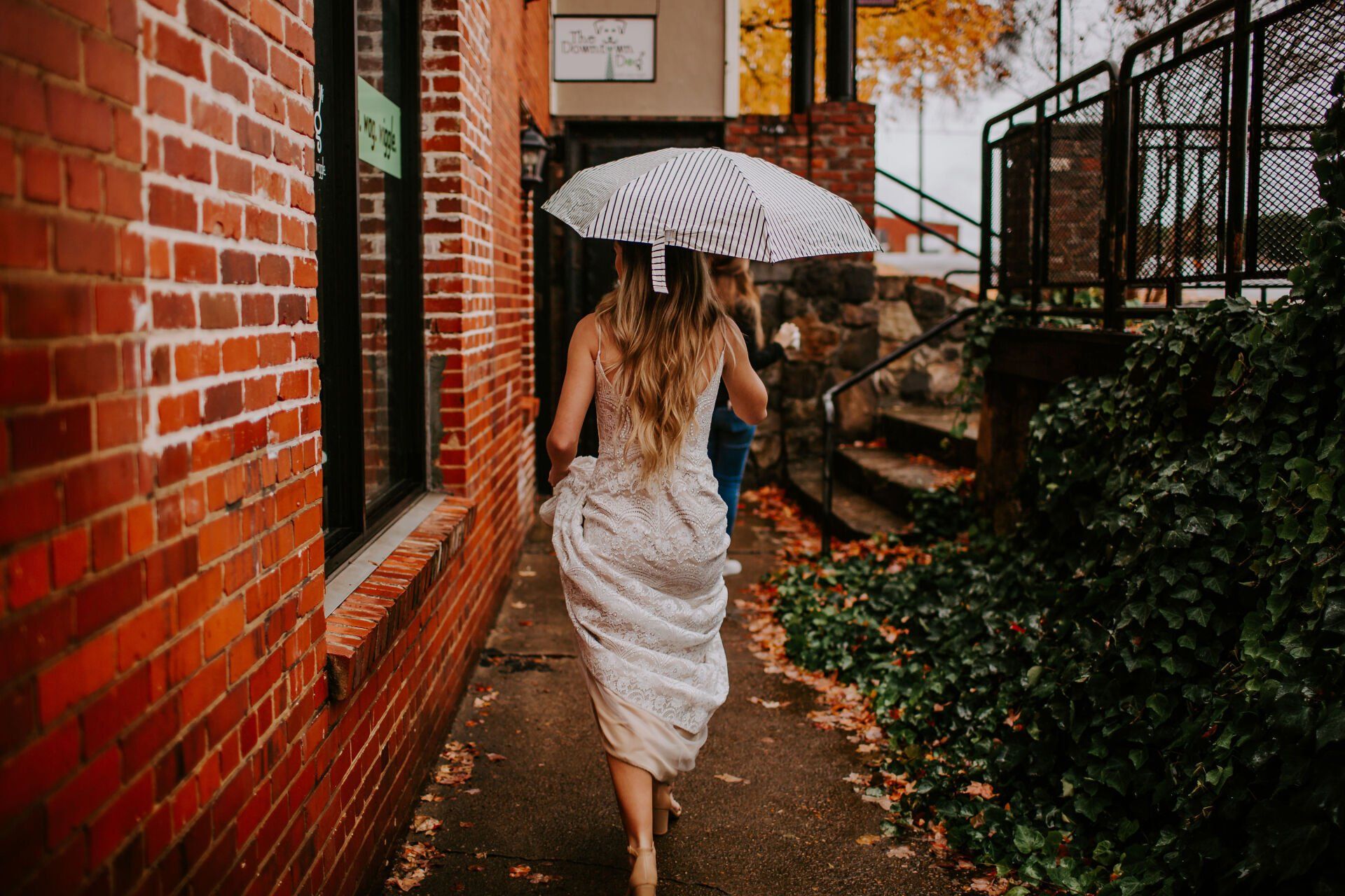 A woman in a wedding dress is walking down a sidewalk with an umbrella.