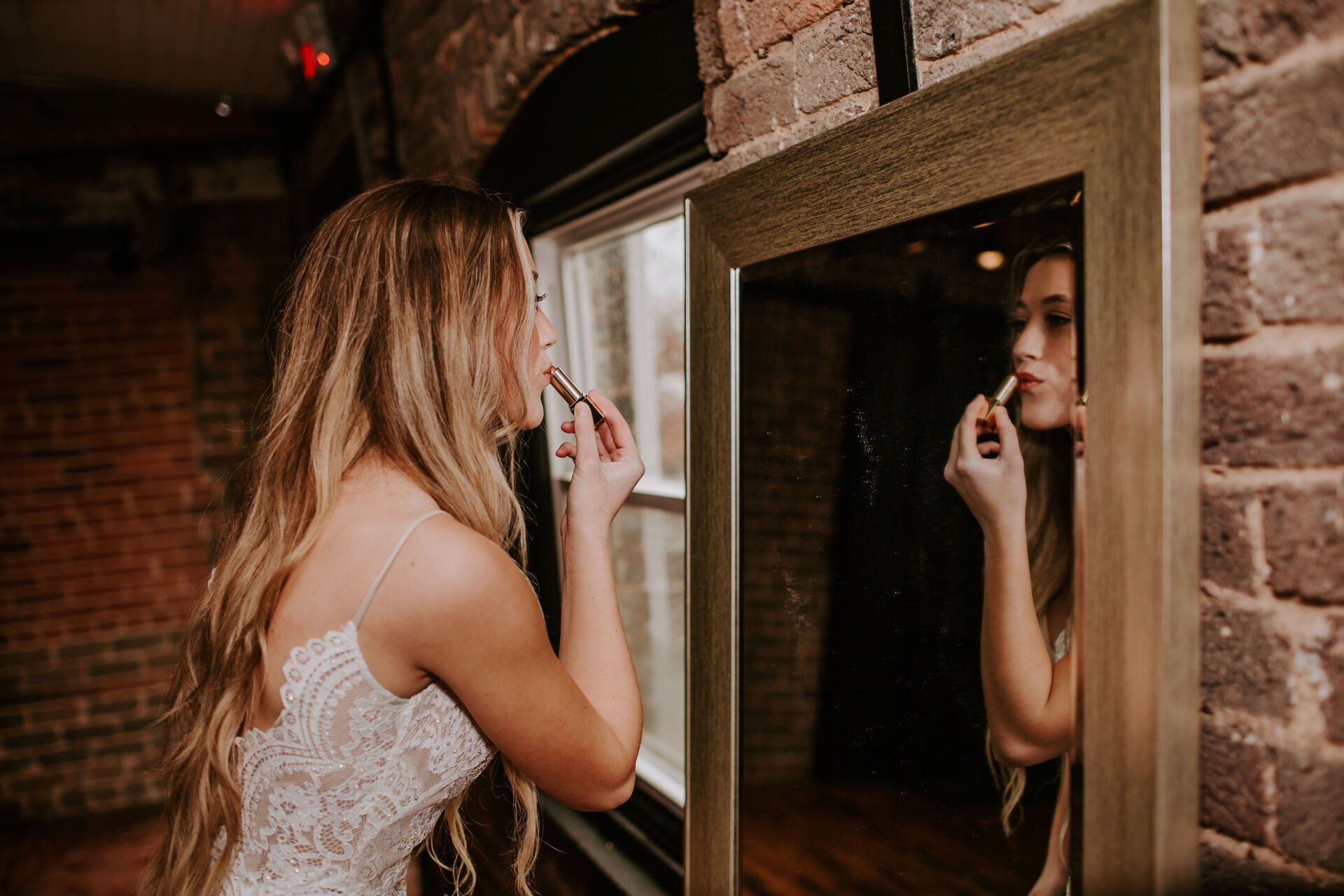 A woman in a wedding dress is applying lipstick in front of a mirror.
