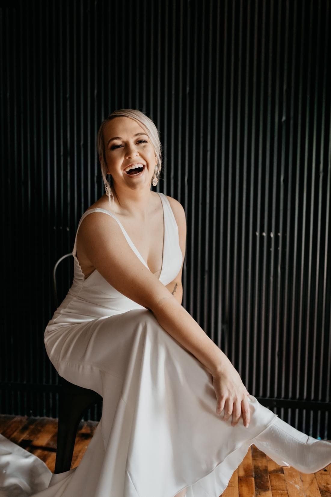 A woman in a white dress is sitting on a chair and smiling.