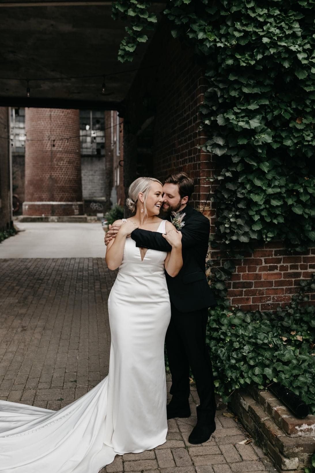 A bride and groom are kissing in front of a brick wall.
