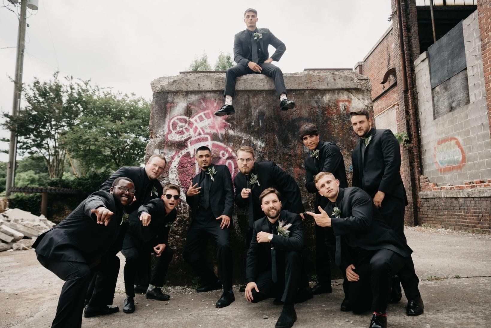 A group of men in suits are posing for a picture in front of a graffiti covered wall.