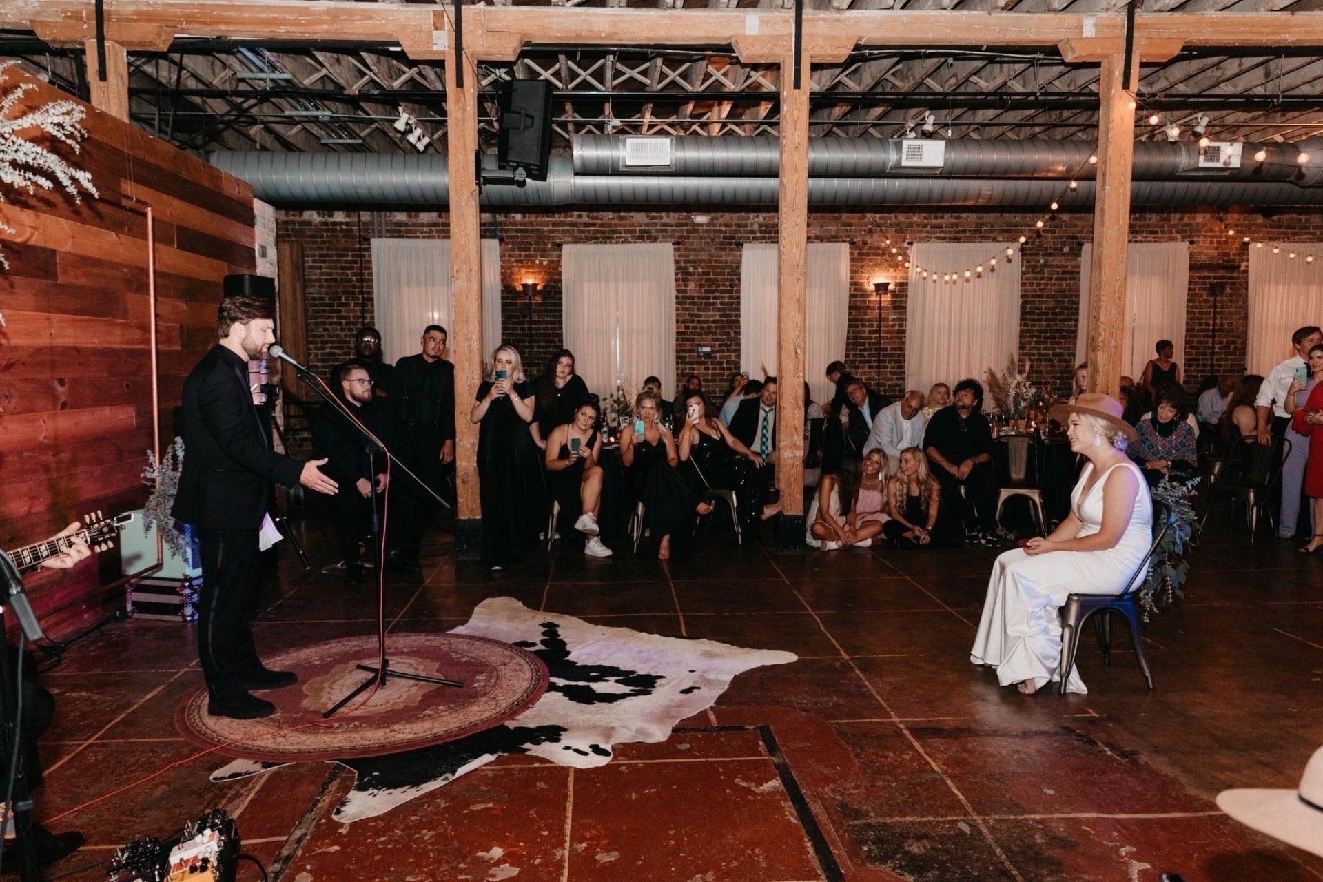 A bride and groom are sitting on a chair in front of a microphone at a wedding reception.