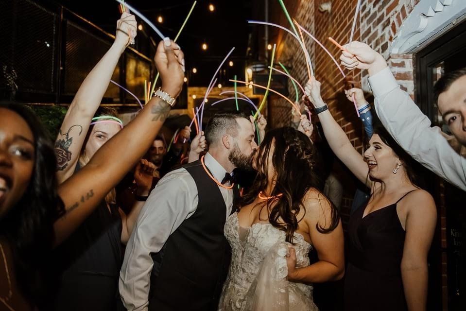 A bride and groom are kissing while their wedding guests hold glow in the dark sparklers.