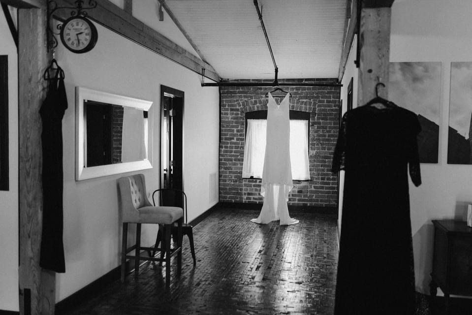 A black and white photo of a bride 's wedding dress hanging in a room.