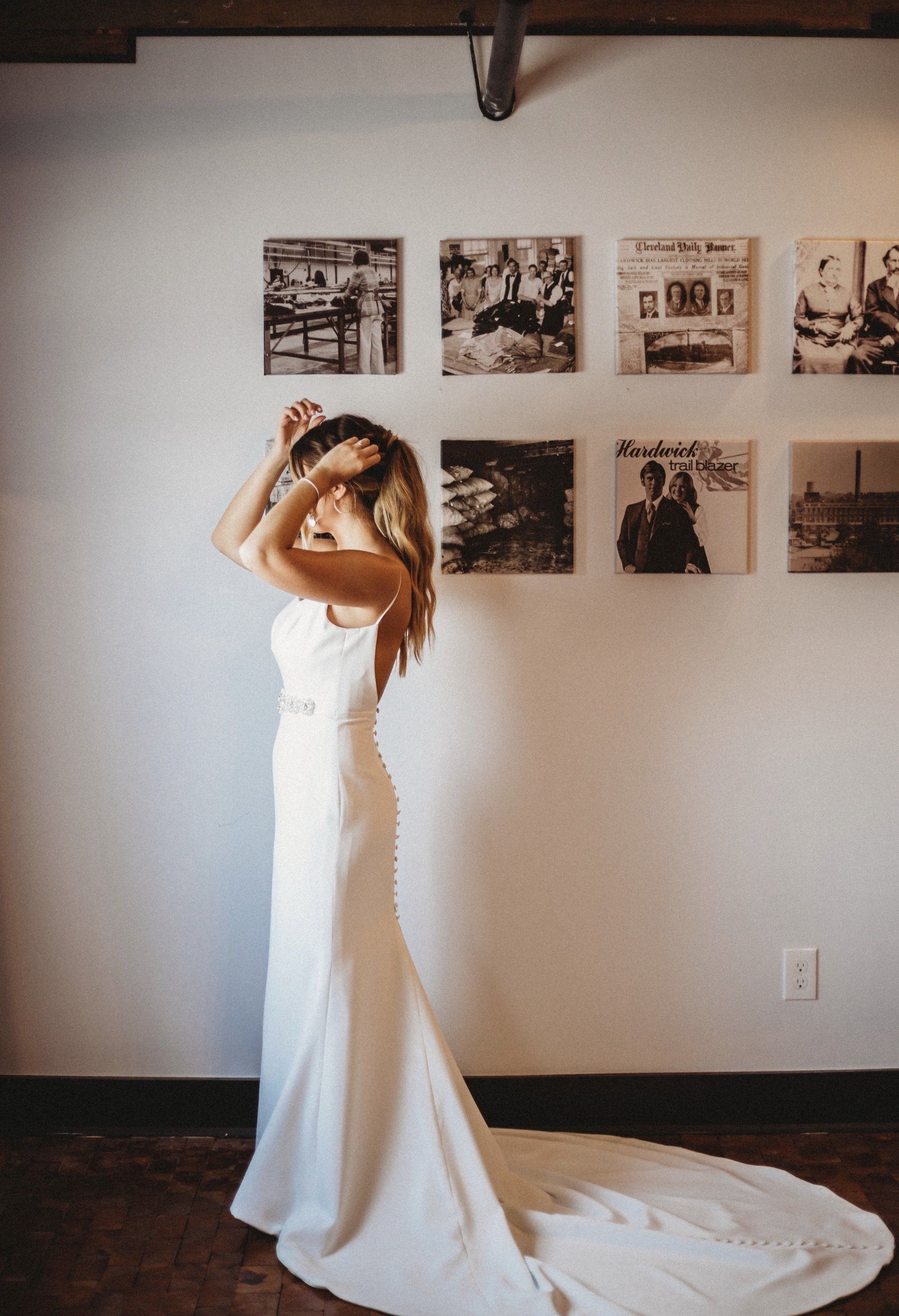A woman in a white dress is standing in front of a wall with pictures on it.