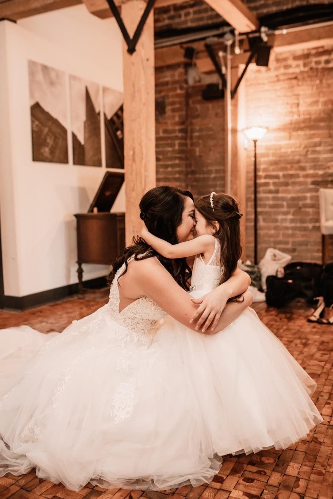 A bride and her flower girl are hugging each other on the floor.