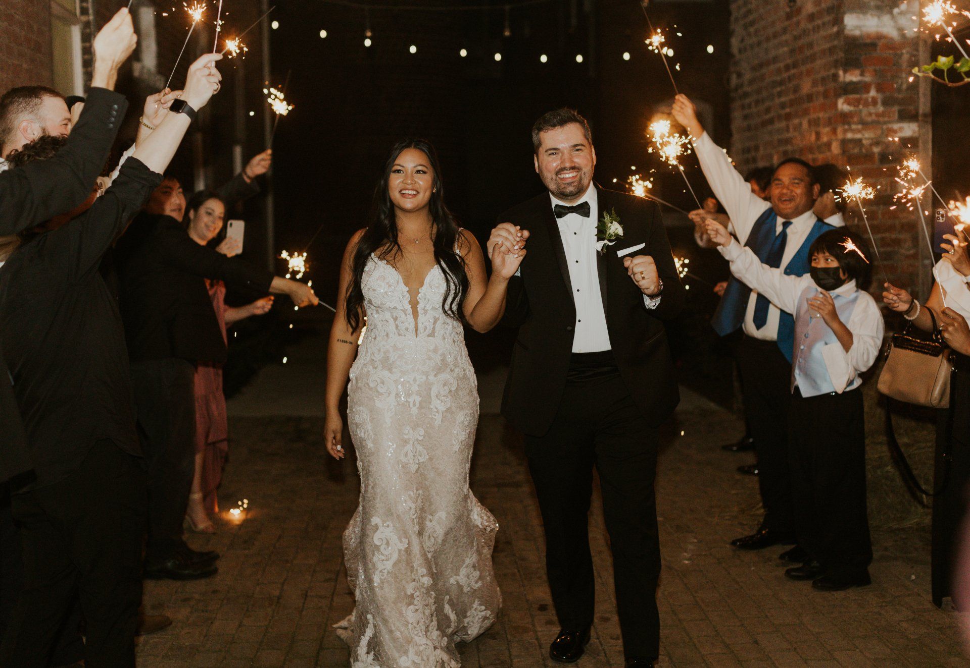 A bride and groom are walking through a crowd of people holding sparklers.