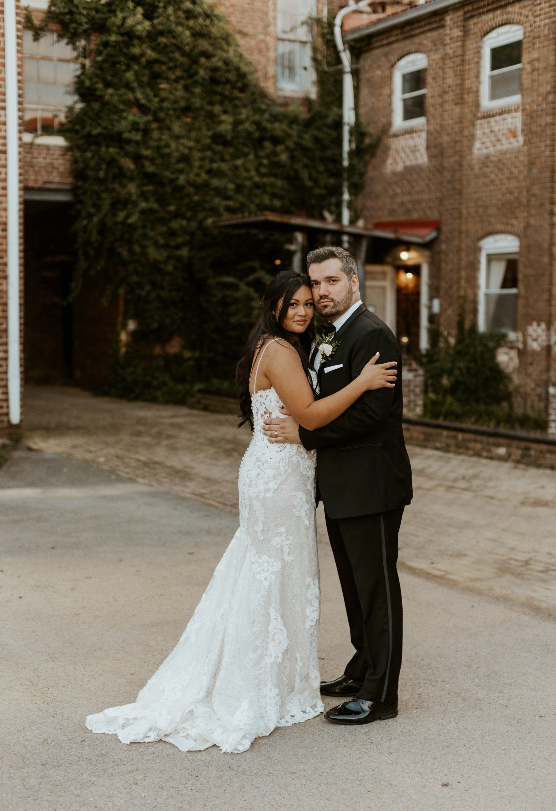 A bride and groom are posing for a picture in front of a brick building.