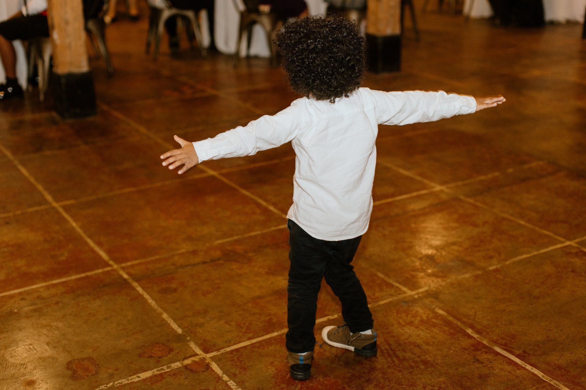 A young boy is dancing on a tiled floor with his arms outstretched.