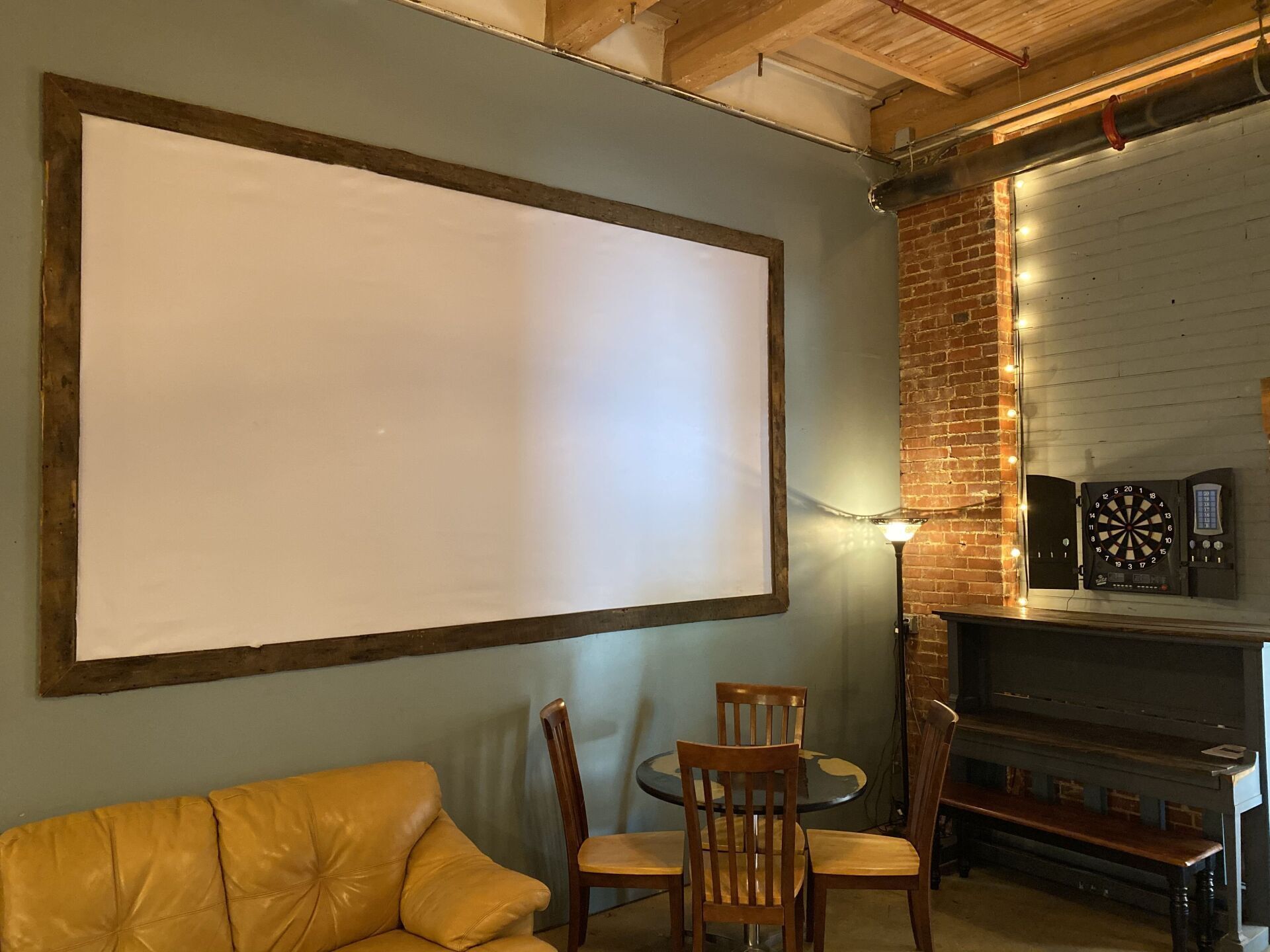 A living room with a couch , table , chairs and a dart board.