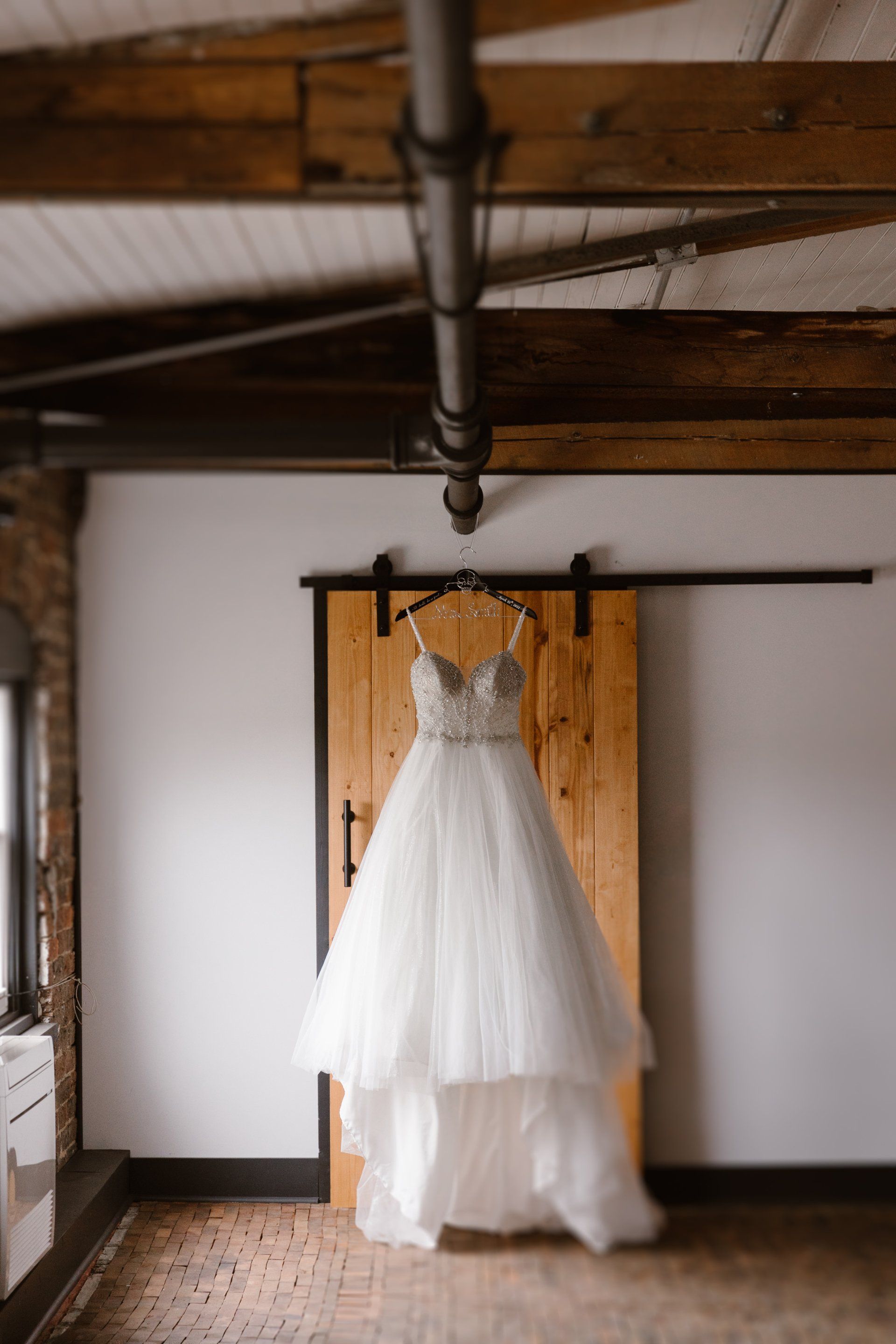 A wedding dress is hanging on a sliding barn door in a room.