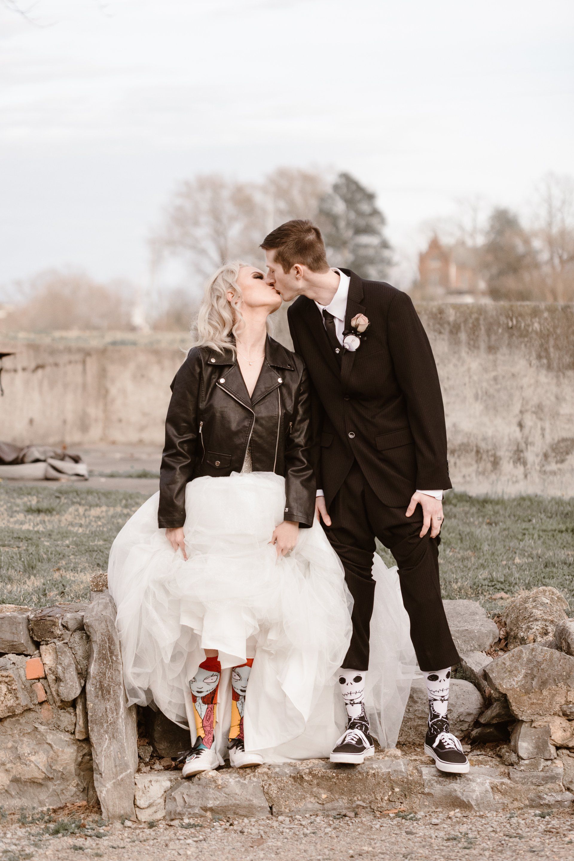 A bride and groom are kissing while standing next to each other on a rock wall.