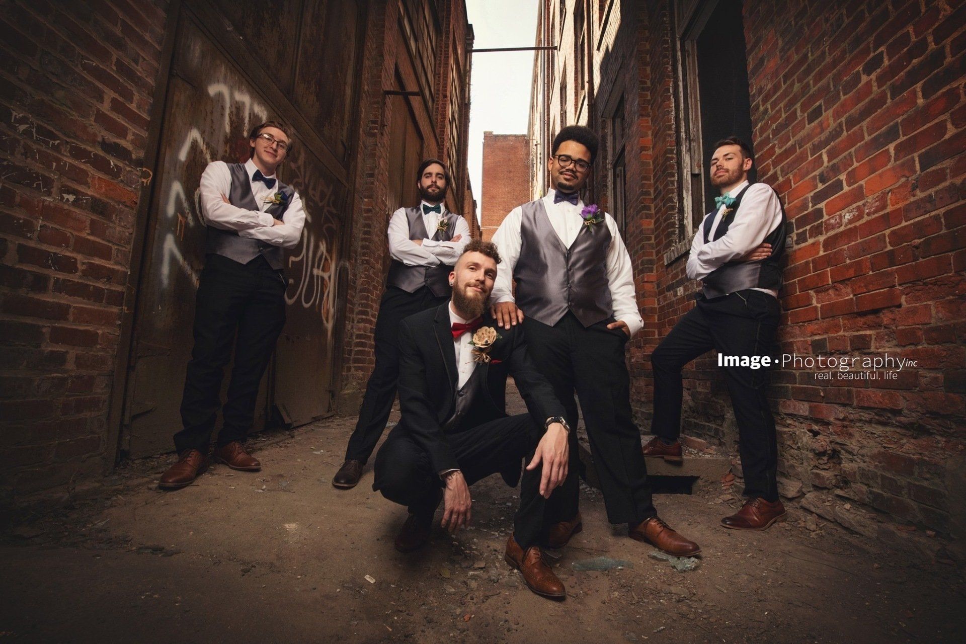 A group of men in suits and bow ties are posing for a picture in an alleyway.