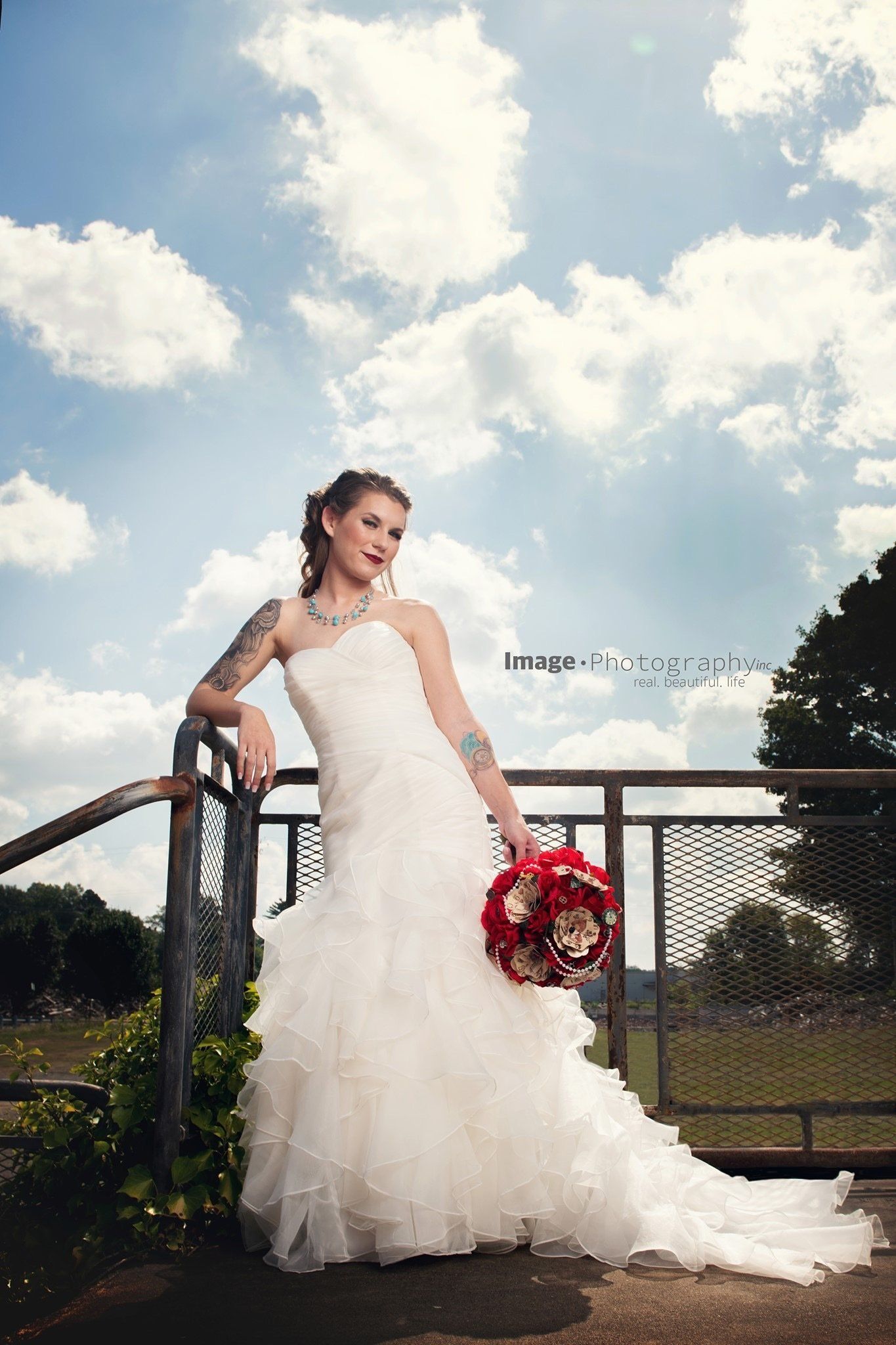 A woman in a wedding dress is leaning on a railing holding a bouquet of flowers.