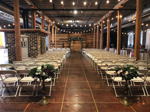 A large room filled with folding chairs and flowers for a wedding ceremony.