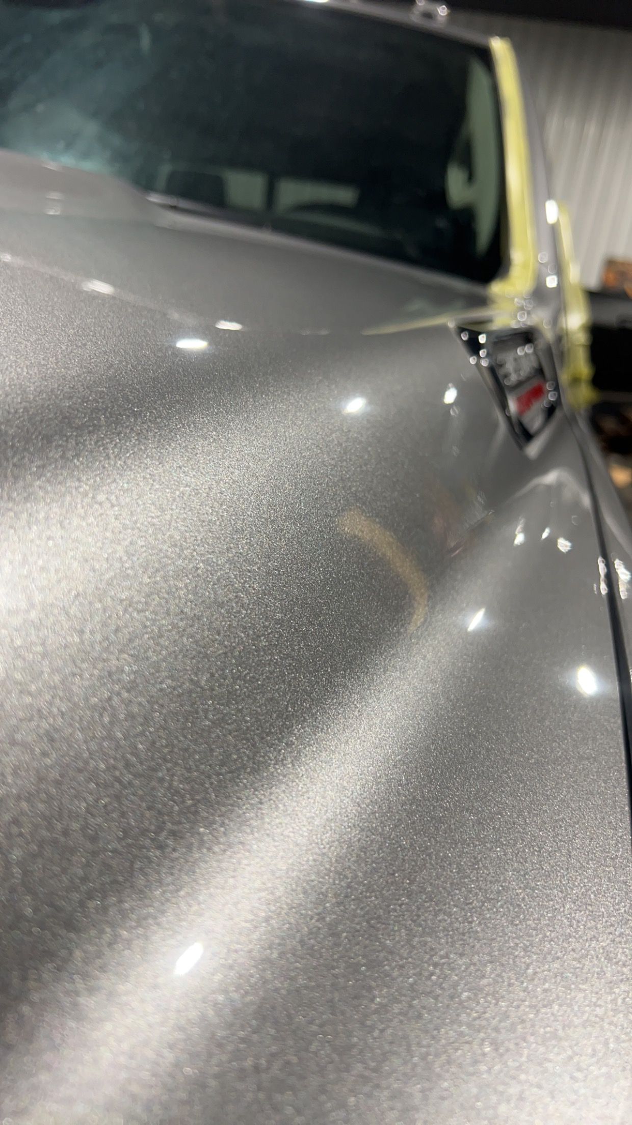 A close up of the hood of a silver car in a garage.