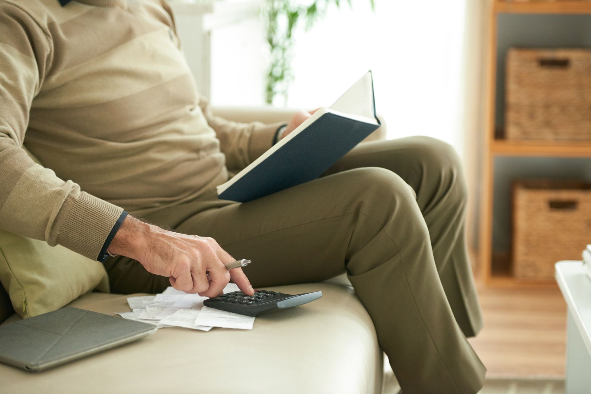 Person in a white shirt using a calculator at a wooden desk, writing and reviewing financial data.