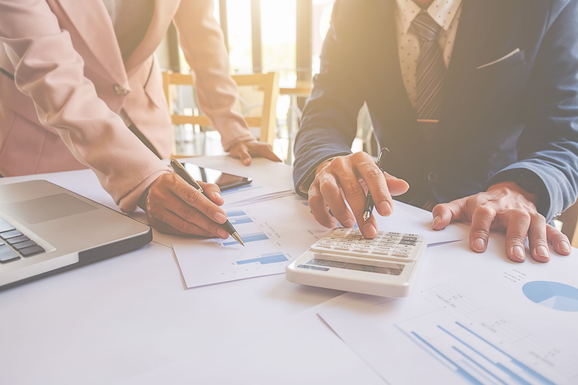 Businesspeople analyzing data with a calculator, documents, and laptop on a table.