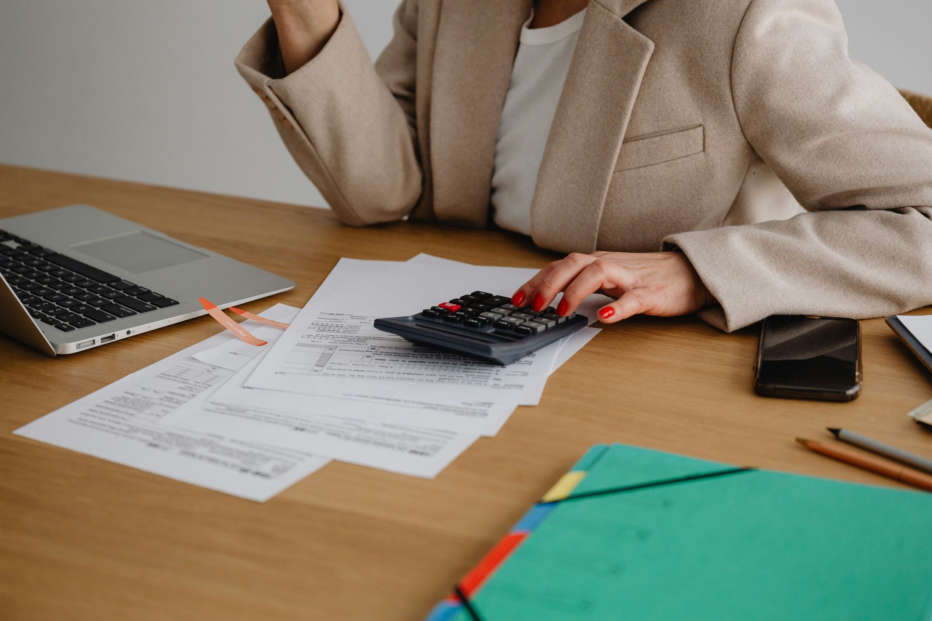 Person in a white shirt using a calculator at a wooden desk, writing and reviewing financial data.